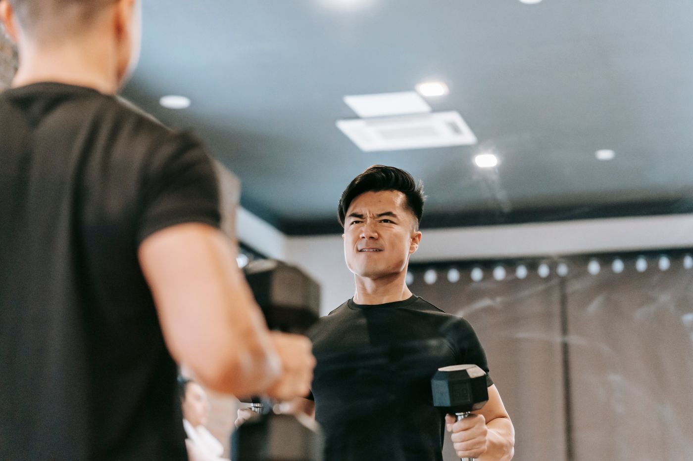 Mężczyzna trenujący biceps z hantlami przed lustrem